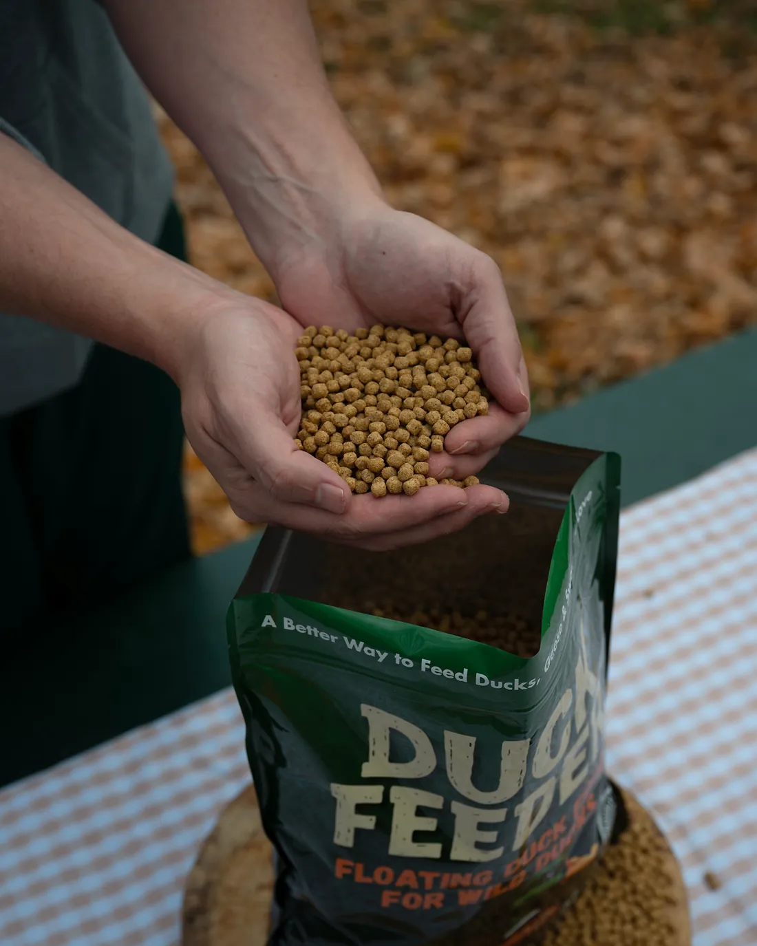 Two hands holding floating duck food pellets over the open Duck Feeder bag
